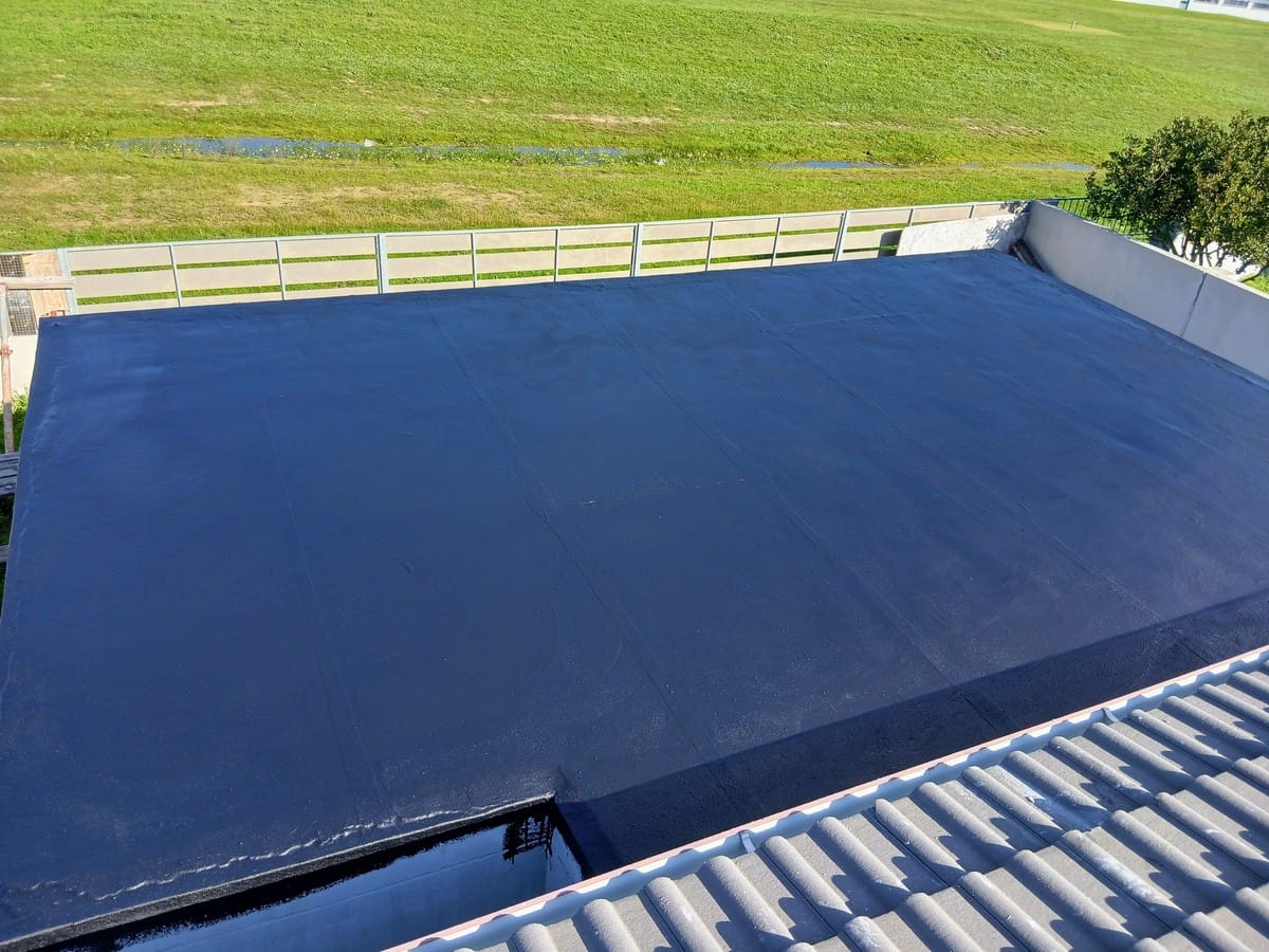 Flat concrete roof slab in Gordon's Bay sealed with a dark blue waterproofing membrane, tile roof in the foreground