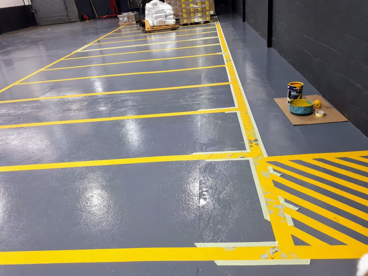 Yellow forklift lane markings freshly painted on a grey factory floor in Somerset West, masking tape still in place